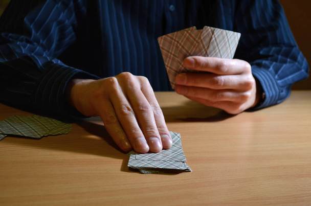 Человек в темноте держит в руках набор игральных карт и берет одну из них, бизнес-стратегию, концепцию конкуренции
 - Фото, изображение