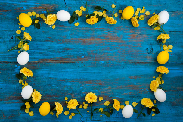 Frame made of yellow flowers and eggs on a blue wooden background. Easter, spring, summer concept. Flat lay, top vie - Zdjęcie, obraz