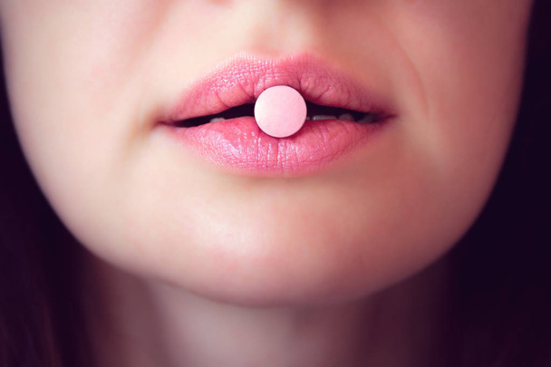 roze tablet in de mond van de vrouw, close-up gezicht - Foto, afbeelding