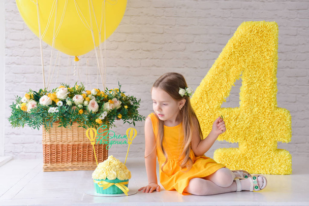 Birthday girl 4-5 years old is celebrating birthday in a decorated stylized studio, number 4 and big balloon. Yellow style. The inscription on the cake rerevod from Russian: Happy birthday - Zdjęcie, obraz