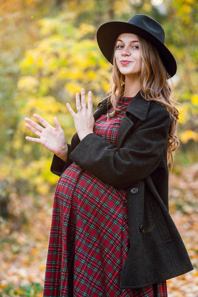 公園で秋の美女。黄色の葉がたくさん。グレーのコートと赤いドレスの女の子。手の腹を保持している妊娠中の女の子 - 写真・画像