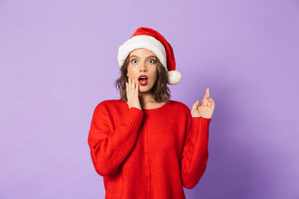 Image of an excited shocked young woman wearing christmas hat isolated over purple background pointing. - Φωτογραφία, εικόνα