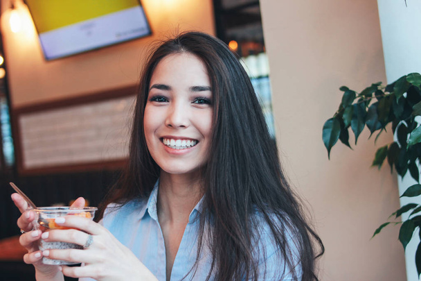 Beautiful charming brunette smiling Asian girl has Breakfast with coffee and Chia pudding at cafe - Foto, Imagem