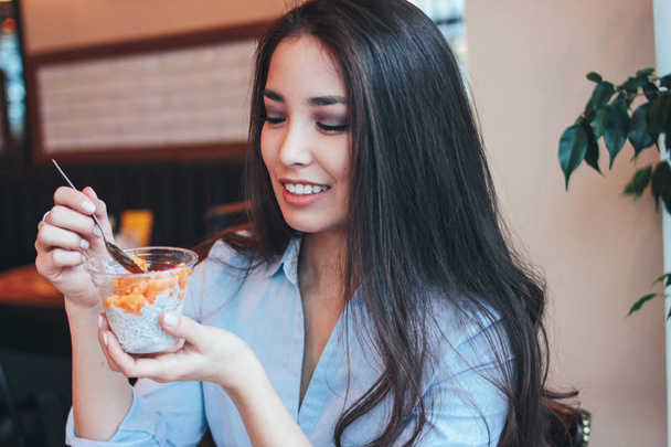 Beautiful charming brunette smiling Asian girl has Breakfast with Chia pudding at cafe - Photo, image
