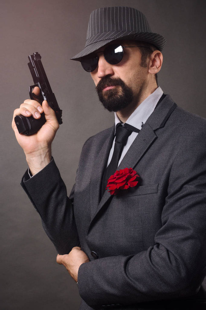 Staromodny eleganckiego mężczyzny w garniturze, kapelusz i okulary w ręku trzyma pistolet. - Zdjęcie, obraz