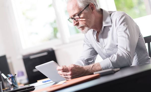 Homme d'affaires senior utilisant une tablette numérique au bureau
 - Photo, image