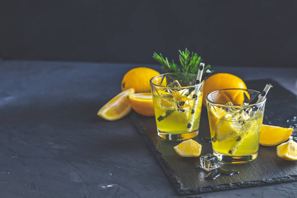 Λεμόνι αλκοόλ πίνουν κοκτέιλ με πάγο, λεμόνι και δεντρολίβανο βότανο στη μαύρη πέτρα τσιμεντένια επιφάνεια. Παραδοσιακό ιταλικό σπιτικό λεμόνι αλκοόλη ποτό limoncello λικέρ. - Φωτογραφία, εικόνα