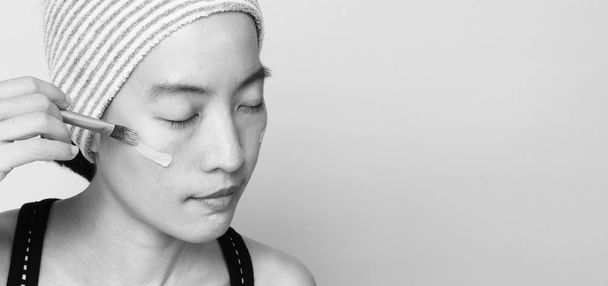 Ασιατική κοπέλα ή γυναίκα 40 ετών όμορφο πρόσωπο με ιαπωνική εμφάνιση συνθέτουν με βάση υγρό και καλλυντικό πινέλο σε ευαίσθητο δέρμα για να βοηθήσει την επιδερμίδα της φαίνονται άψογη και δεν retouch. - Φωτογραφία, εικόνα