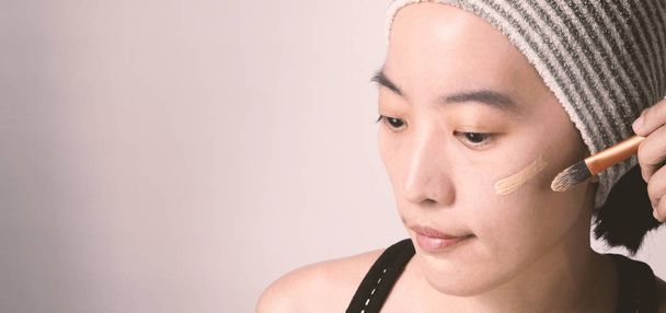 Aasian tyttö tai nainen 40-vuotias kaunis kasvot japanilainen ilme muodostavat säätiön neste ja kosmeettinen harja herkkä iho auttaa hänen ihonväri näyttää virheetön eikä korjailla. - Valokuva, kuva
