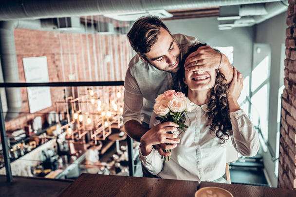 Surprise for you! Beautiful romantic couple in cafe. Young man is presenting flowers to his wife. - Photo, image