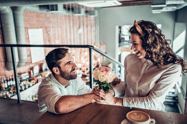 True feelings. Beautiful romantic couple in cafe. Man is presenting flowers to his wife. - Photo, Image