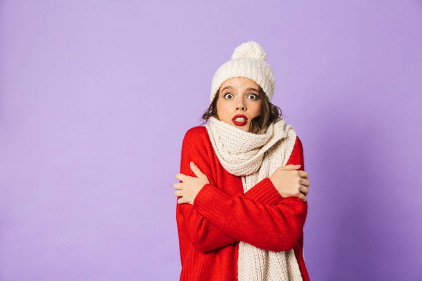 Portrait of a young frozen woman wearing winter hat and scarf isolated over purple background. - Foto, immagini