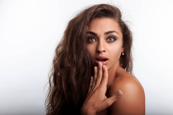 Person looks surprised. Female model posing on camera on the white background. Portrait of pretty young woman with long curly wavy brown hair.  - 写真・画像