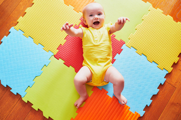 Happy smiling baby girl lying on colorful play mat on the floor, view from above - Fotó, kép