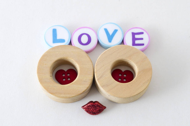 Slovo láska z barevné zaoblené gumy a dvě dřevěné kruhy s srdíčka červené tlačítko a malý červený šplhat rty proti bílým pozadím - Fotografie, Obrázek