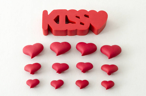 De kus woord en kleine rode harten tegen witte achtergrond. Valentijnsdag decoratie - Foto, afbeelding