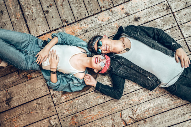 Young and carefree.Top view of happy young couple looking at sky and smiling while lying on wooden floor. - Photo, Image