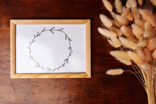 Painted wreath on the paper in the frame and flowers on the brown wooden background. - Fotografie, Obrázek