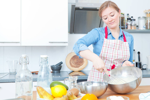 attractive young woman in apron preparing dough in kitchen - Foto, afbeelding