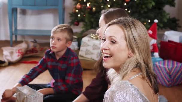 Mother sitting on floor with children as they opening Christmas gifts together - shot in slow motion - Video