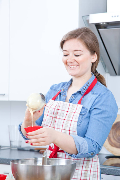 uśmiechnięta młoda kobieta w fartuch, przygotowując pyszne babeczki w kuchni - Zdjęcie, obraz