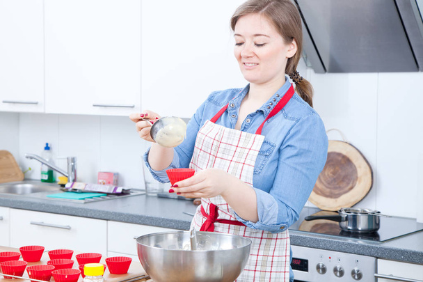 smiling young woman in apron preparing delicious cupcakes in kitchen - Foto, immagini