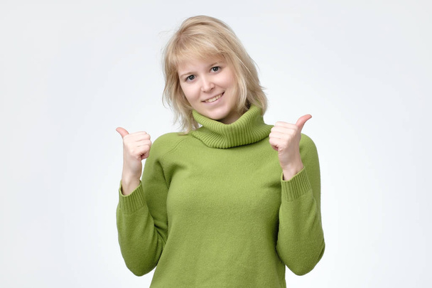 Happy young caucasian female wearing green sweater making thumb up sign and smiling cheerfully - Foto, afbeelding