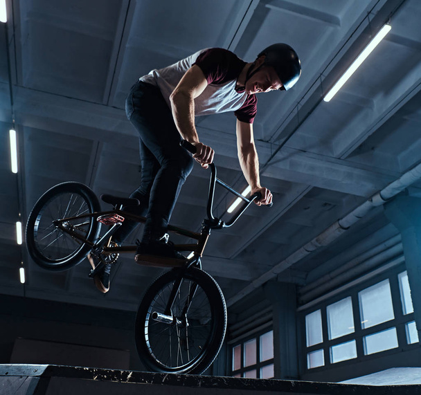 Young man with BMX performing tricks in skatepark indoors - Fotoğraf, Görsel