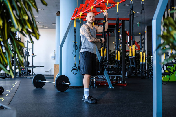 Wytatuowany mężczyzna sportowiec trzyma fitness zawieszenie liny w siłowni - Zdjęcie, obraz