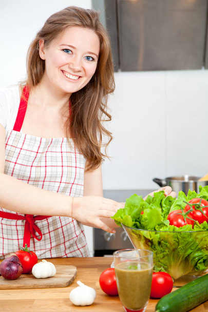 beautiful happy young woman preparing healthy food with vegetables and smiling at camera in kitchen - Foto, afbeelding