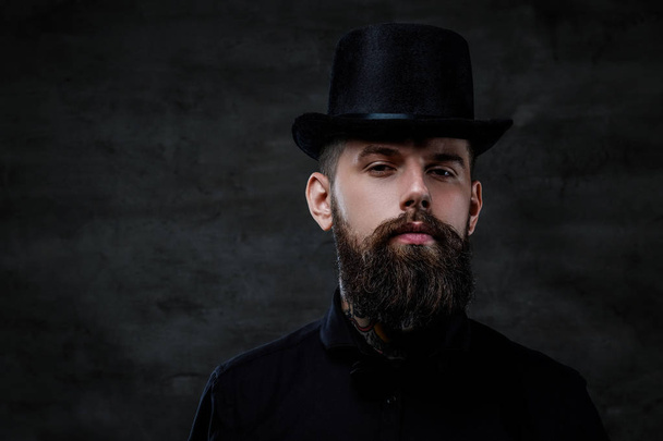 Retrato de um homem barbudo à moda antiga com tatuagens no pescoço usando um chapéu superior, isolado em um fundo escuro. Estúdio
 - Foto, Imagem
