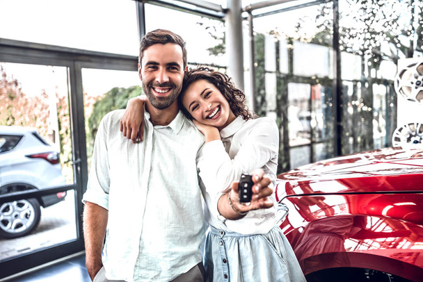 Adventure awaits. Beautiful happy young couple hugging holding the keys to their new car smiling joyfully at the dealership - Foto, Bild