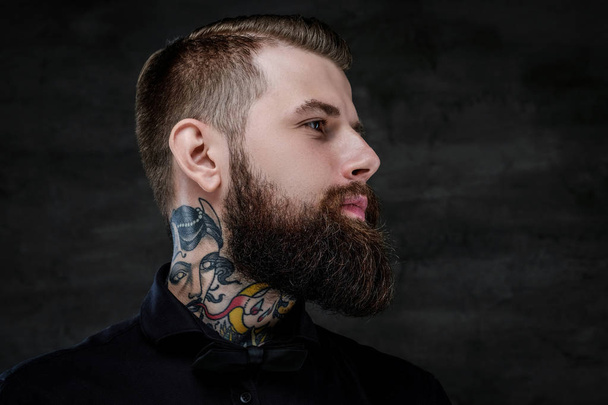 Profiel portret van een expressieve bebaarde man met tatoeages op zijn nek, geïsoleerd op een donkere achtergrond. - Foto, afbeelding