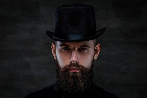 Un serio uomo barbuto vecchio stile che indossa un cappello a cilindro, guardando una macchina fotografica, isolato su uno sfondo scuro
.  - Foto, immagini