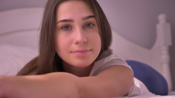 Closeup portrait of young stunning caucasian female lying on the bed and looking at camera smiling - Кадры, видео