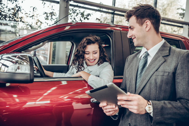車情報。デジタル タブレットのカップルを購入車サービスに情報を示す車サロン専門のセールスマンでは新しい車に座って幸せな若い女を助けるコミュニケーション クライアント ビジネス コンセプト - 写真・画像
