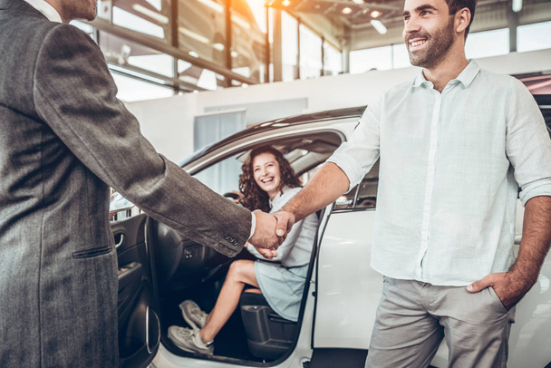 close up view of handshake of salesmen with the man in the showroom on the background of a woman in a new car. - Φωτογραφία, εικόνα
