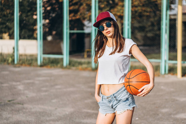 Pretty young sporty girl with basketball ball outdoor - Fotó, kép