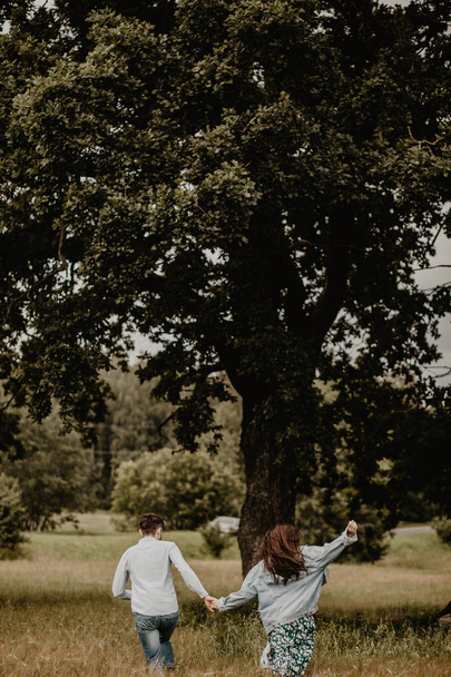 Outdoor shot of young couple walking through meadow hand in hand  - Foto, imagen