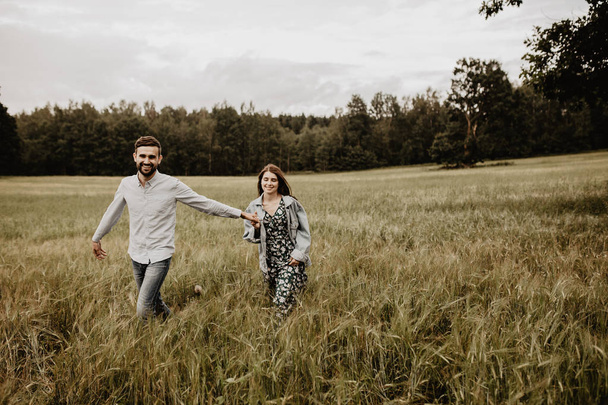 Outdoor shot of young couple walking through meadow hand in hand  - Фото, изображение