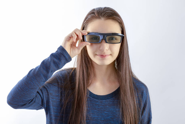 Hymyilevä teini tyttö, jolla on 3D-lasit, katselee kameraa valkoisella taustalla. Elokuvakonseptin katsominen
. - Valokuva, kuva