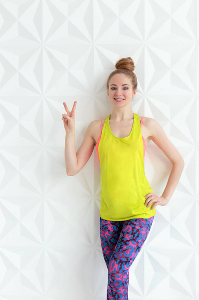 Sporty young woman showing victory sign over white wall - Foto, imagen