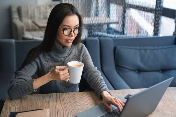 Portret kobiety atrakcyjny biznes filiżankę kawy w jej ręka które pracują nad jej laptop w urzędzie - Zdjęcie, obraz