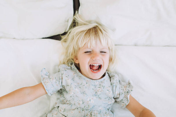 Cute little girl resting and smiling on a bed at home. Leisure.   - Fotografie, Obrázek