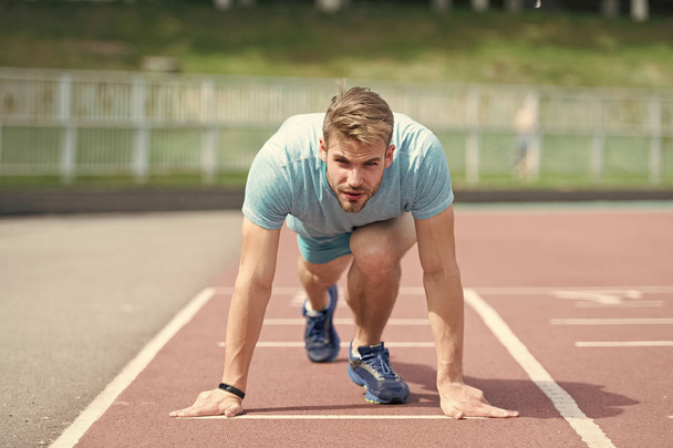 Man runner on start position at stadium. Runner in start pose on running surface. Man run outdoor at running track. Sport and athletics concept. Sportsman on concentrated face ready to go - Fotoğraf, Görsel
