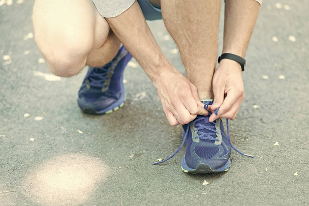 Getting ready to jogging. Hands tying shoelaces sneaker, road background. Hands of sportsman with pedometer tying shoelaces sporty sneaker. Running equipment concept. Shoelaces tying by male hands - Photo, image
