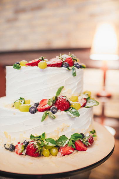 dreiteilige nackte Hochzeitstorte mit Früchten und Beeren. weiße Hochzeitstorte mit Erdbeeren und Beeren. - Foto, Bild