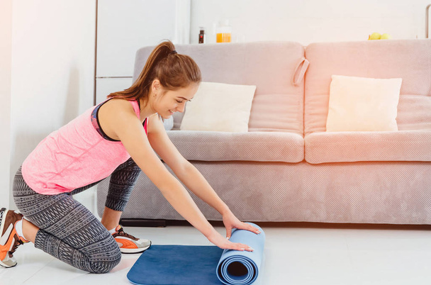 Young woman with yoga mat indoors, preparing for exercise, unrolling or rolling yoga mat - Foto, imagen