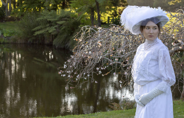 Mujer eduardiana vestida con conjunto blanco y un sombrero en un jardín
 - Foto, Imagen