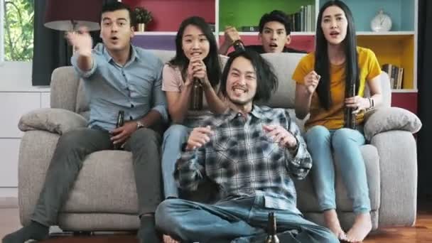 Group of friends watching tv together on sofa. Mixed race young people enjoying watching tv, cheering. House party concept. - Video